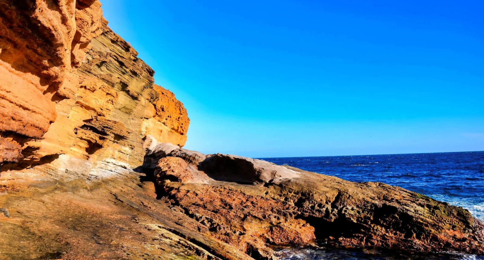 Acantilados rojizos junto a un mar azul bajo un cielo despejado.