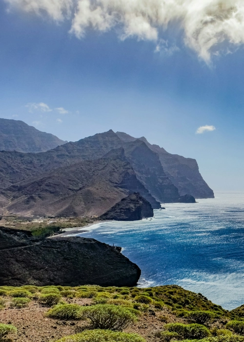 Acantilados junto al mar bajo un cielo azul con nubes dispersas.