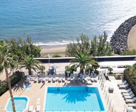 Piscina y playa con palmeras, vistas al mar desde arriba.