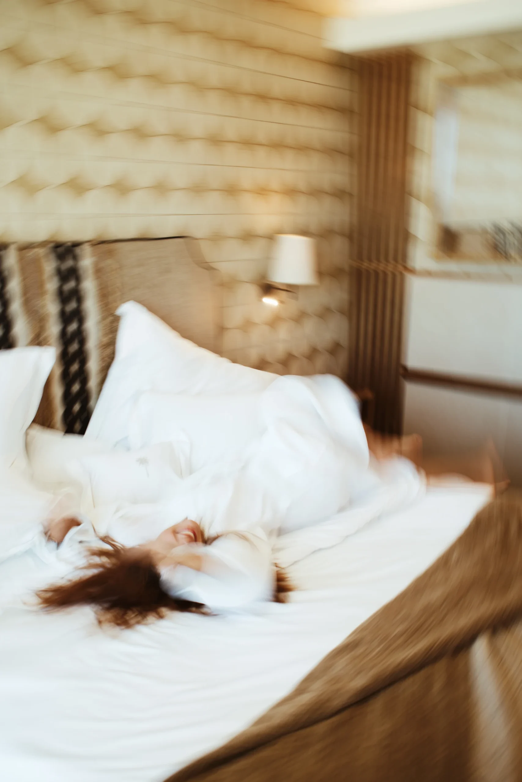 Blurred person joyfully rolling on a bed in a cozy bedroom.