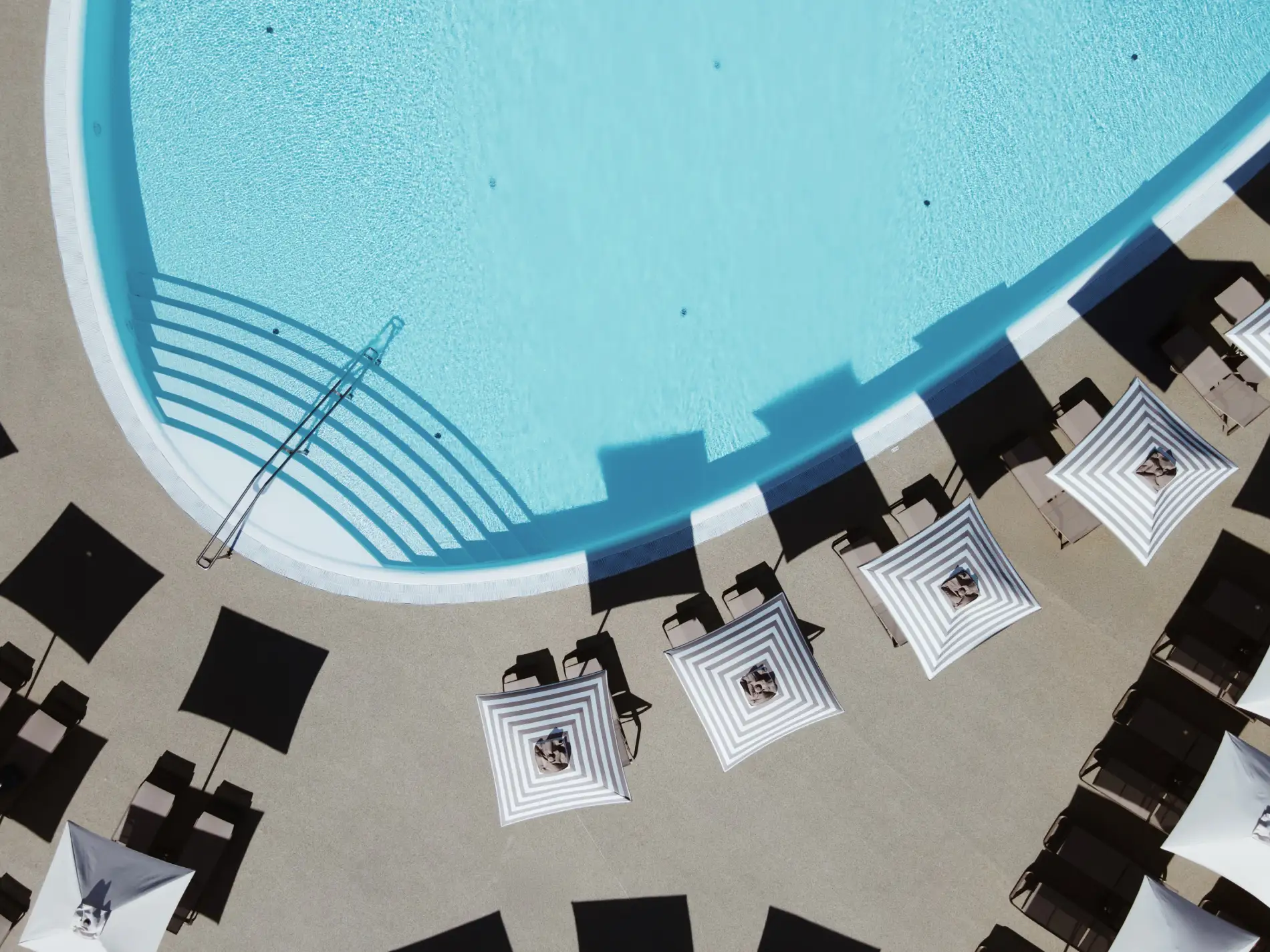 Aerial view of a pool with striped umbrellas and lounge chairs surrounding it.