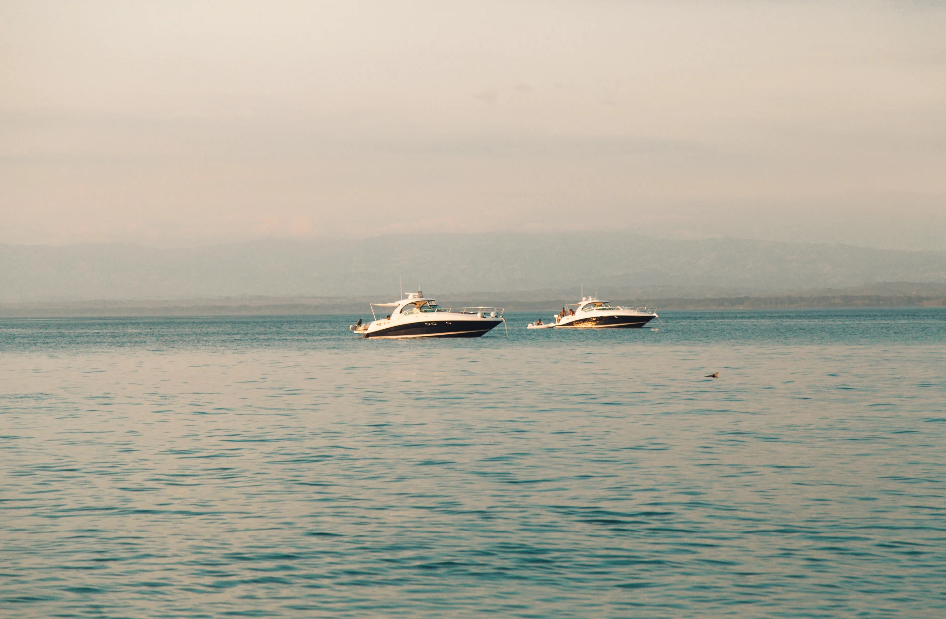 Two yachts floating on a calm sea under a hazy sky.
