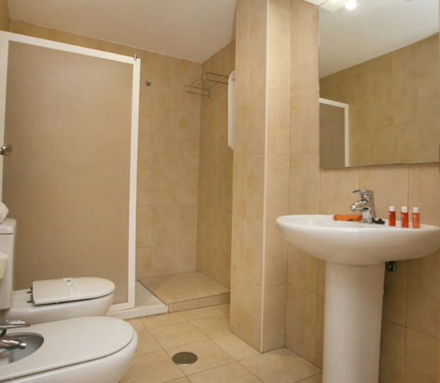 Baño con ducha, inodoro, bidé, lavabo y espejo, decoración sencilla y tonos beige.