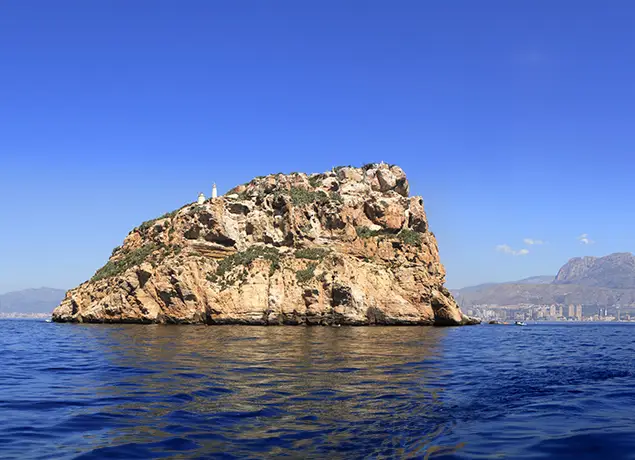 Isla rocosa en el mar bajo un cielo azul despejado. Hay edificios pequeños en la cima.