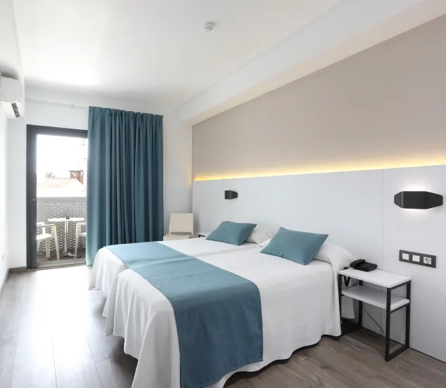 Habitación de hotel moderna con cama doble, decorada en blanco y azul, y acceso a balcón.