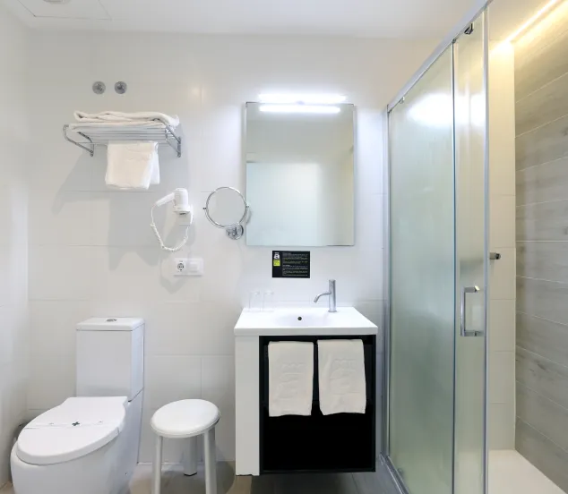 Baño moderno con ducha, espejo, lavabo, inodoro, toallas y secador de pelo.