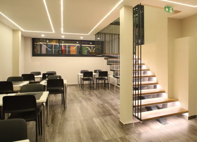Restaurante moderno con sillas y mesas negras, escaleras iluminadas y un diseño interior minimalista.