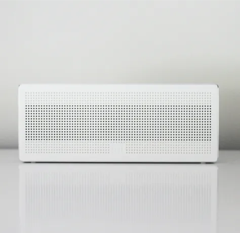 Parlante blanco rectangular con rejilla perforada sobre fondo gris claro.