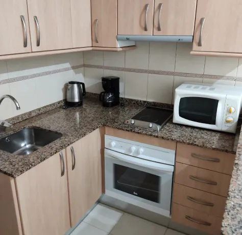 Cocina moderna con electrodomésticos: horno, microondas, cafetera y hervidor en encimera de granito.