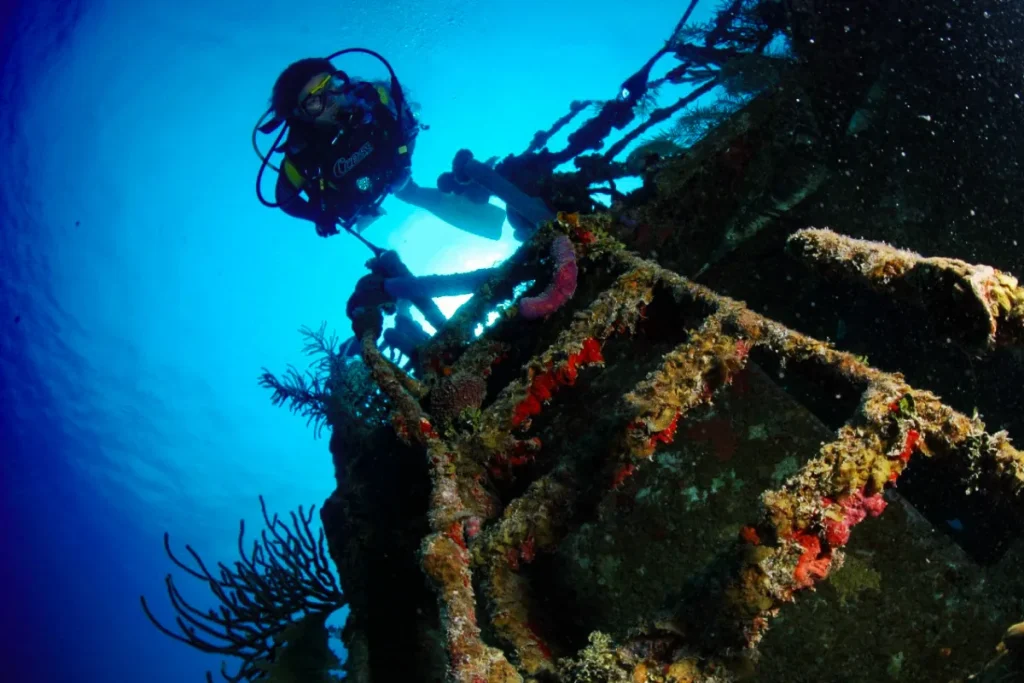 Buzo explorando un arrecife de coral en un barco hundido bajo el agua.