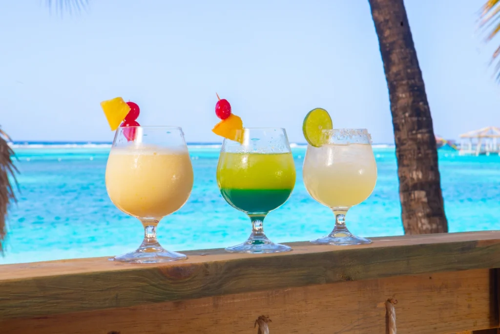 Three tropical cocktails on a wooden ledge by the ocean.