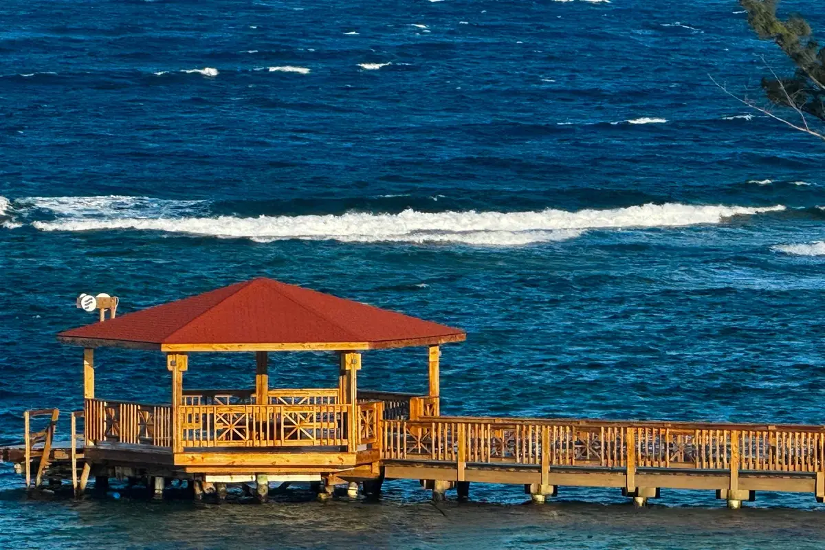 Muelle de madera con techo rojo sobre un mar azul con olas blancas.
