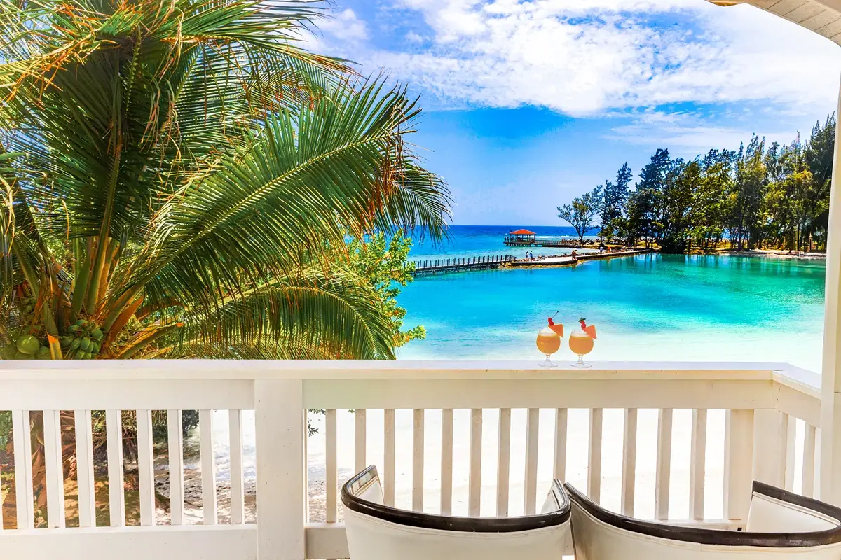 Terraza con dos cócteles frente a un mar turquesa y una palmera.