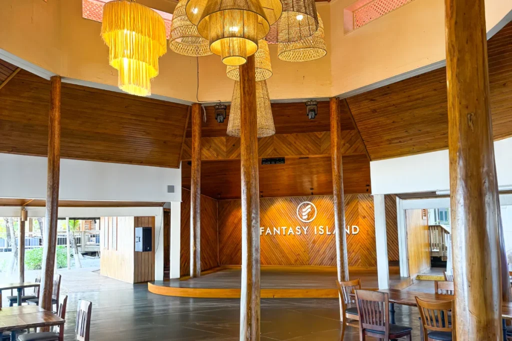 Interior de sala con lámparas colgantes y letrero de "FANTASY ISLAND".