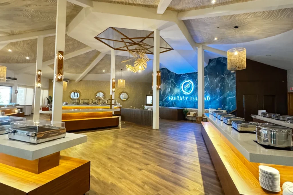 Restaurante moderno con buffet y letrero de "Fantasy Island" iluminado.
