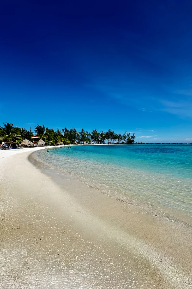 Playa de arena blanca y mar turquesa bajo un cielo despejado y azul.