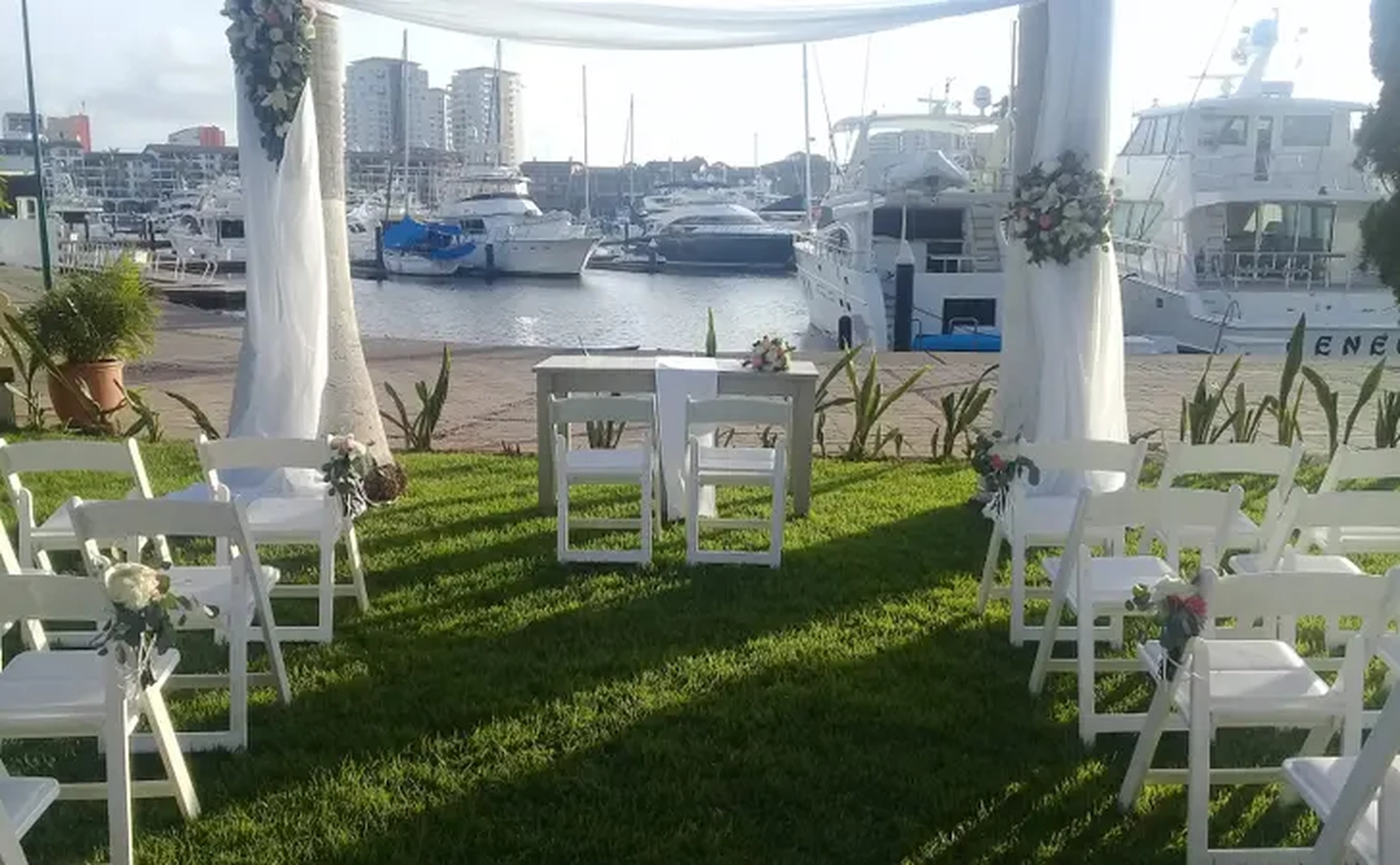 Ceremonia de boda al aire libre junto a un muelle, con sillas blancas y decoración floral.