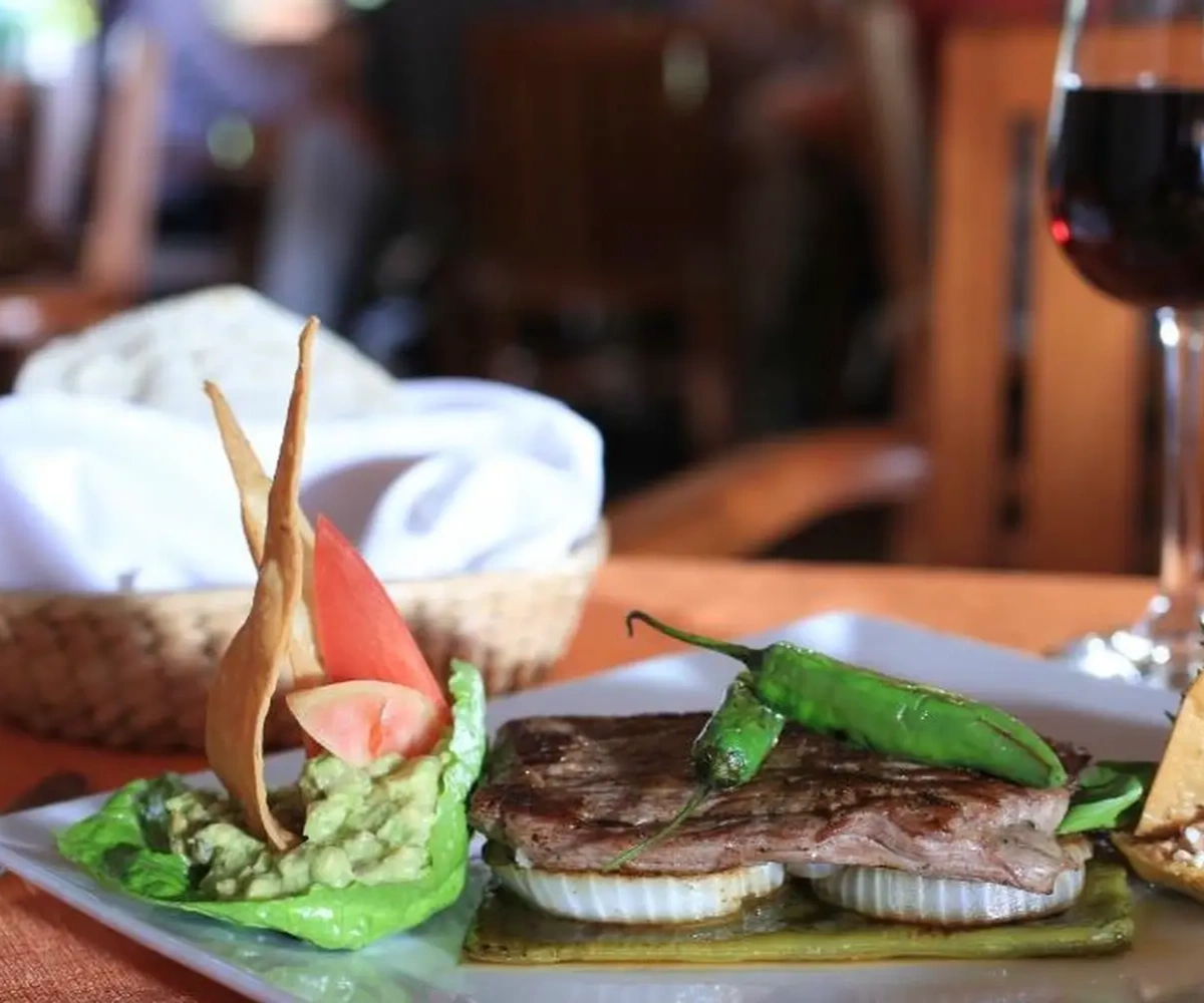 Plato de carne con cebolla, nopal y chile, acompañado de guacamole, totopos y una copa de vino tinto.