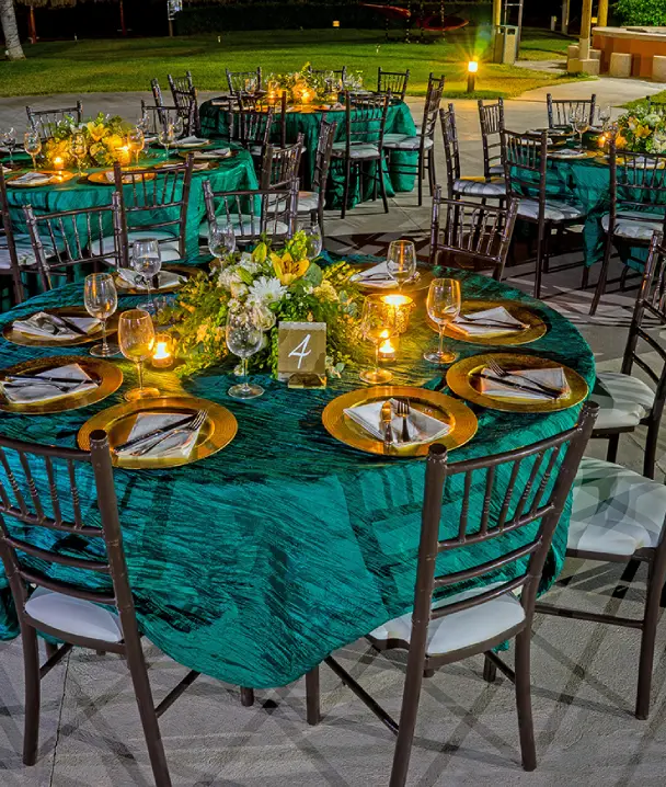 Mesas elegantes con manteles verdes, velas y arreglos florales en un evento al aire libre.