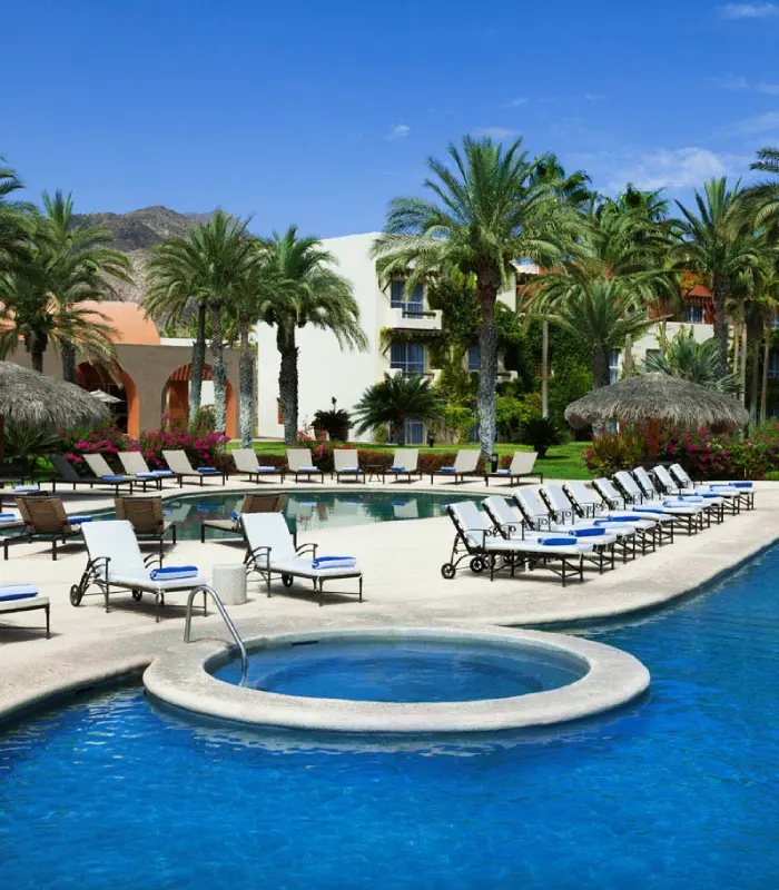 Piscina azul rodeada de palmeras y tumbonas blancas en un ambiente tropical.