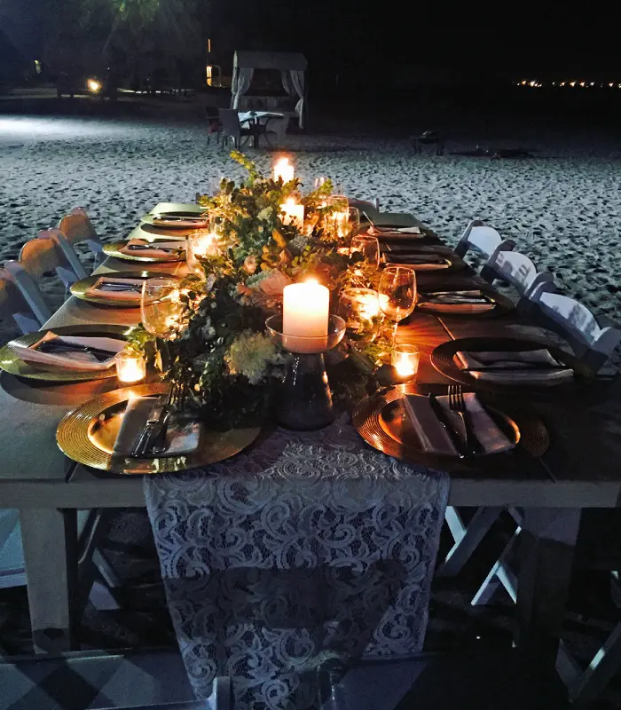 Mesa decorada con velas y flores en una playa de noche.