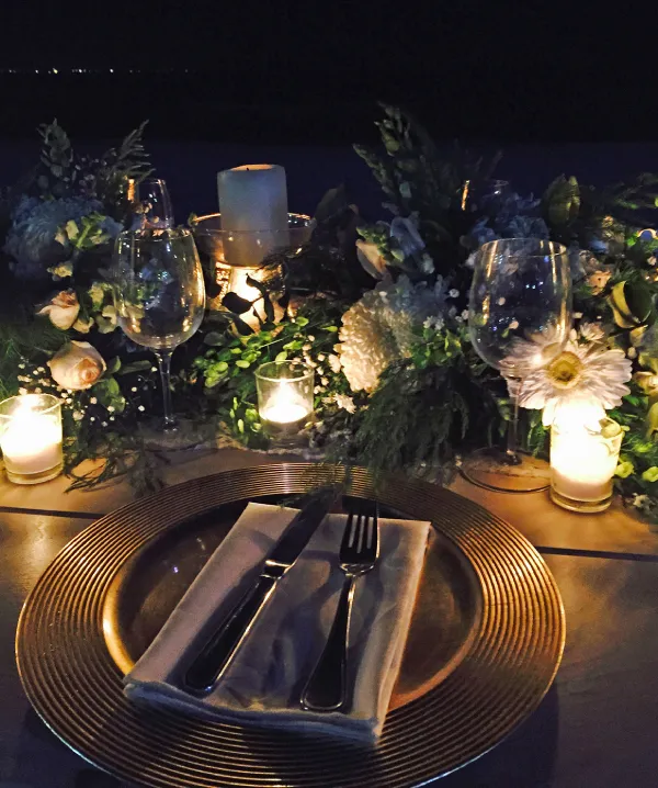 Mesa elegante con platos, copas, velas y flores en decoraci&oacute;n nocturna.