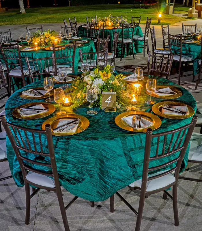 Mesa redonda decorada en tonos verdes, velas iluminando y flores en el centro.