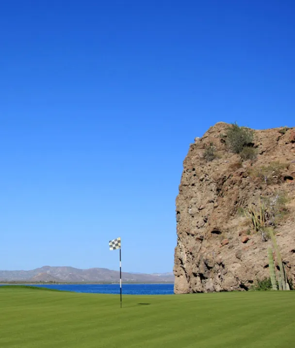 Campo de golf junto al mar, con una gran roca y cielo azul despejado.