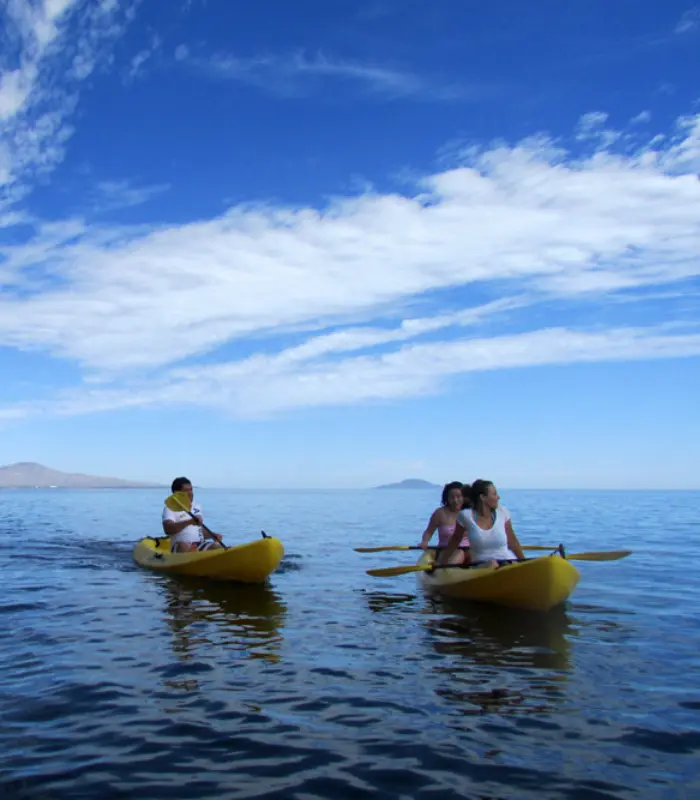 Personas remando en kayaks amarillos sobre un lago, bajo un cielo azul con nubes.