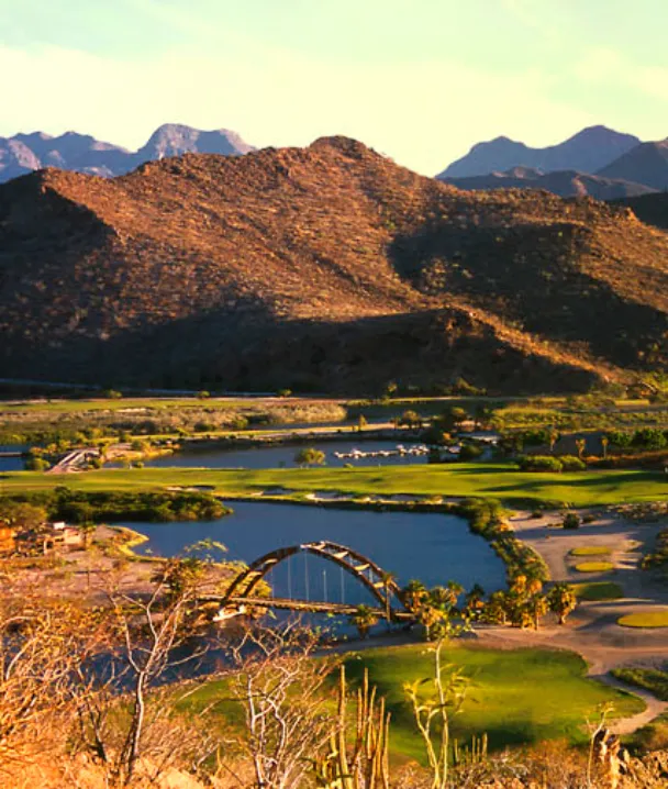 Paisaje monta&ntilde;oso con lagos y puente bajo luz dorada del atardecer.