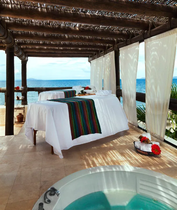 Camas de masaje al aire libre con vista al mar y jacuzzi en un ambiente tropical y relajante.