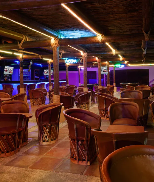 Sala con sillas de cuero y luz de ne&oacute;n en el techo, vista de un bar con pantallas y mesas.