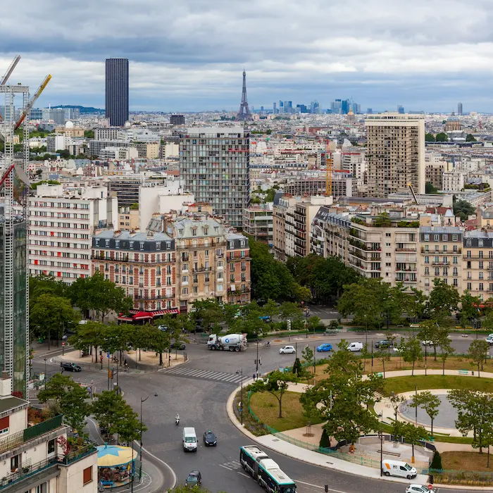 Vue aérienne d'un quartier urbain avec la tour Eiffel en arrière-plan, ciel nuageux.