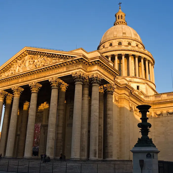 Bâtiment historique avec colonnes et dôme illuminé au crépuscule.