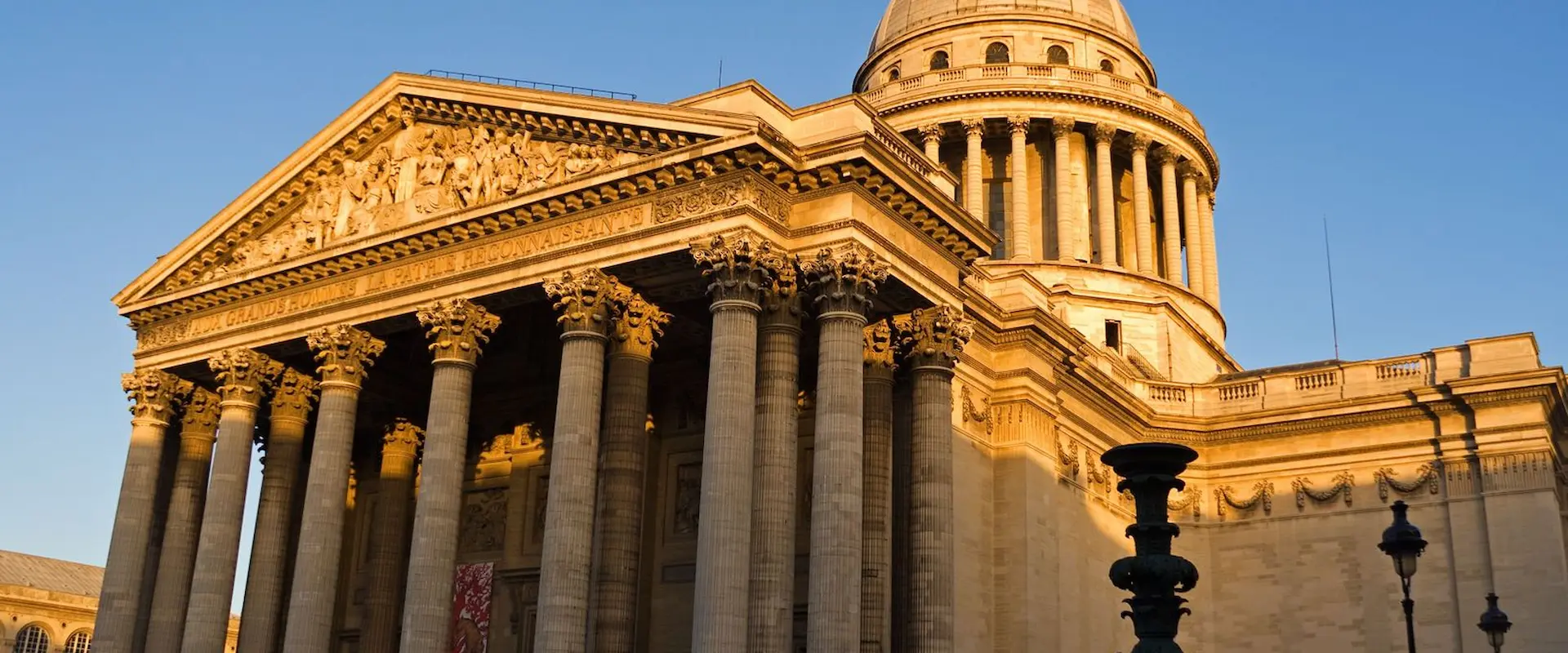 Façade ensoleillée d'un bâtiment historique avec colonnes et dôme imposants.