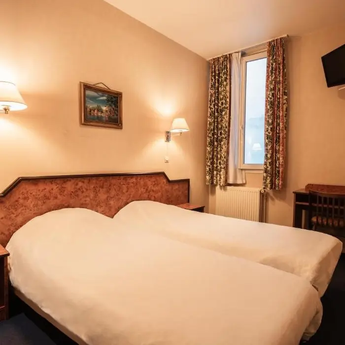 Chambre d'hôtel avec lits jumeaux, lampes murales, tableau et fenêtre.