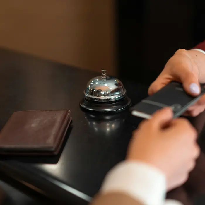 Main tenant un smartphone près d'une sonnette de réception sur un comptoir.