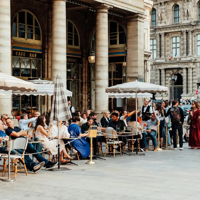 Terrasse de café parisien animée avec des personnes assises sous des parasols.
