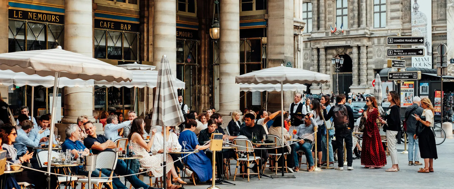 Terrasse de café occupée à Paris, près de la Comédie-Française, avec passants et serveurs.