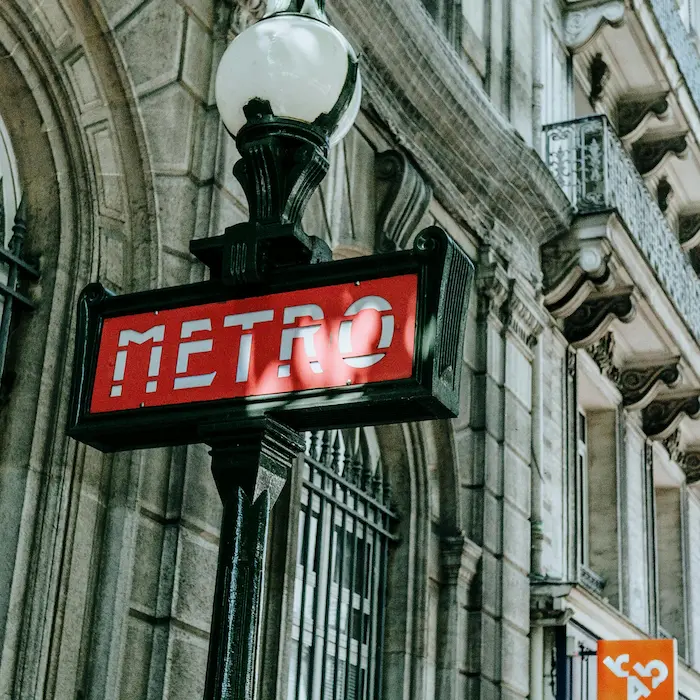 Panneau "METRO" rouge et blanc, devant un bâtiment ancien en pierre.