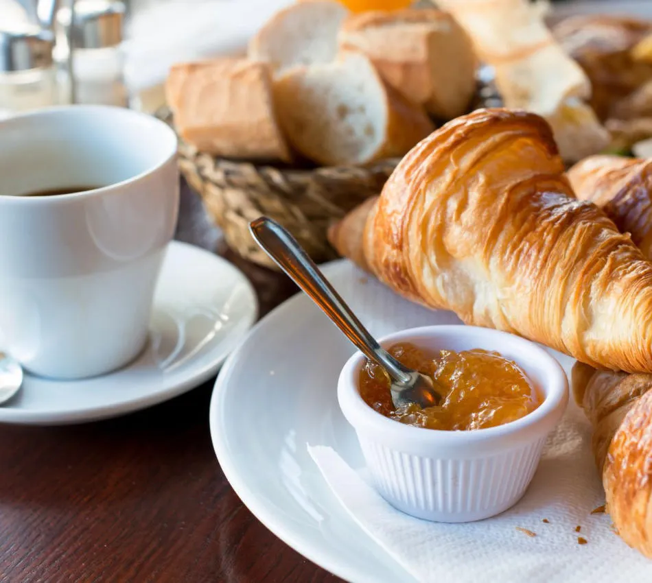 Petit déjeuner avec croissant, confiture, pain et café sur une table en bois.