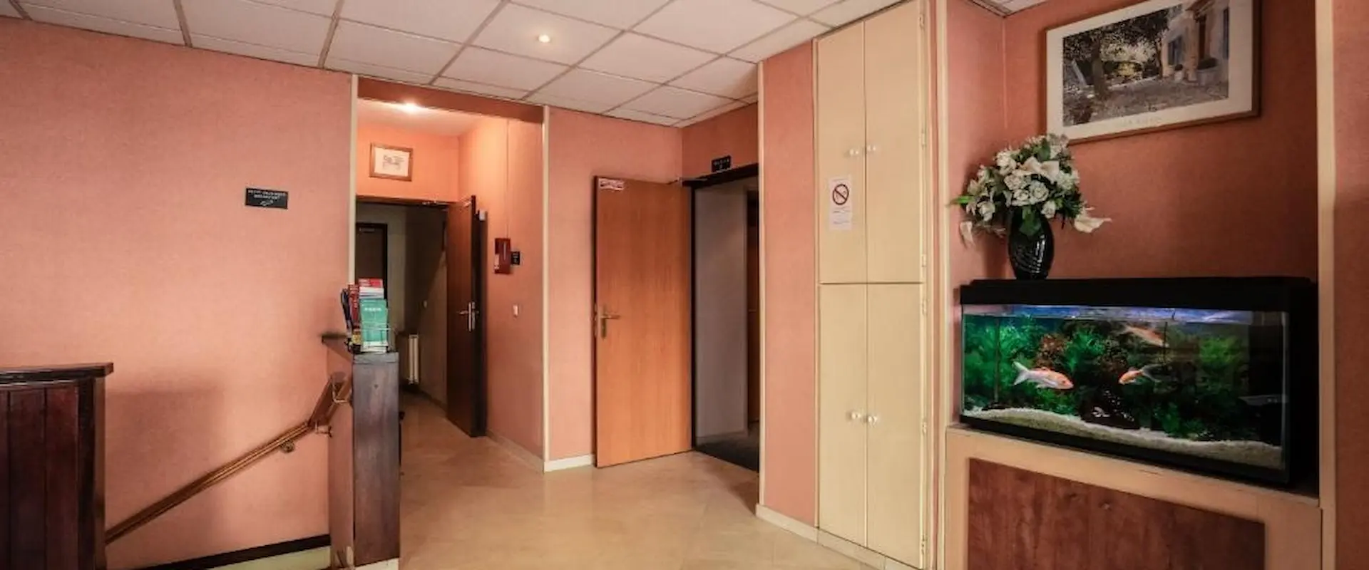 Intérieur avec un aquarium, des fleurs, et des portes boisées dans un couloir à décor rose et beige.