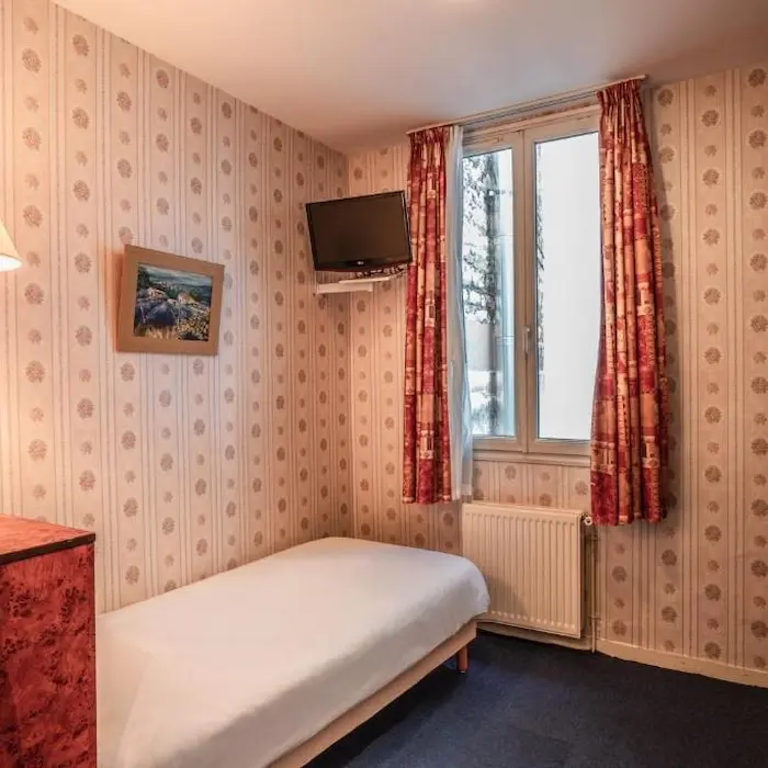 Petite chambre avec un lit simple, télévision murale et fenêtre avec rideaux rouges.