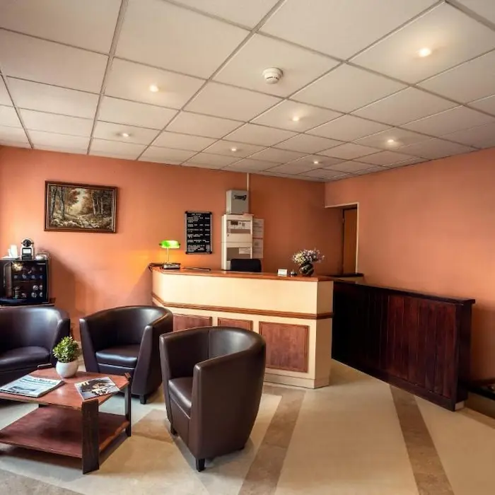 Salon chaleureux avec fauteuils en cuir, table basse et comptoir d'accueil, éclairage doux.