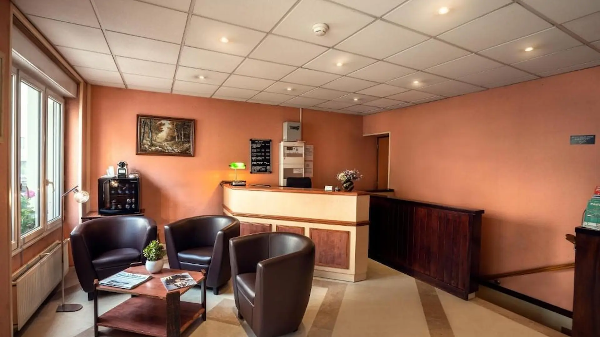 Salle d'attente avec fauteuils marron, comptoir d'accueil, tableau et lampes modernes.