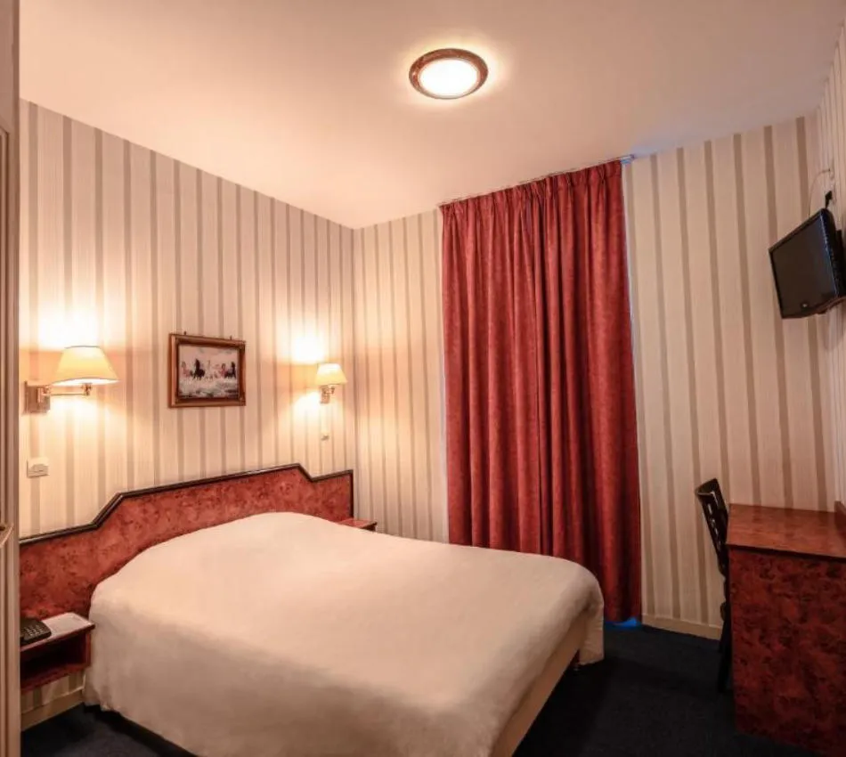 Chambre d'hôtel cosy avec lit double, lampes murales, rideaux rouges et bureau en bois.
