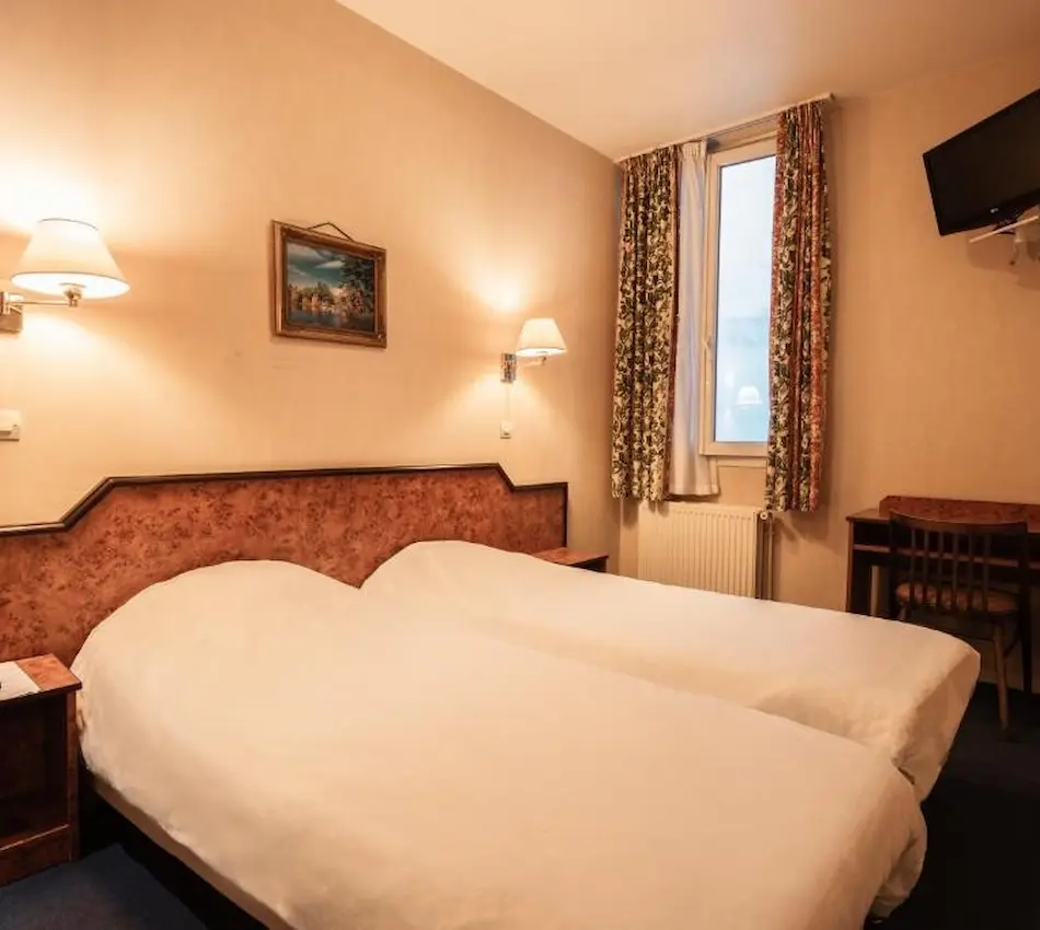 Chambre d'hôtel avec deux lits simples, bureau, TV et lampes murales.