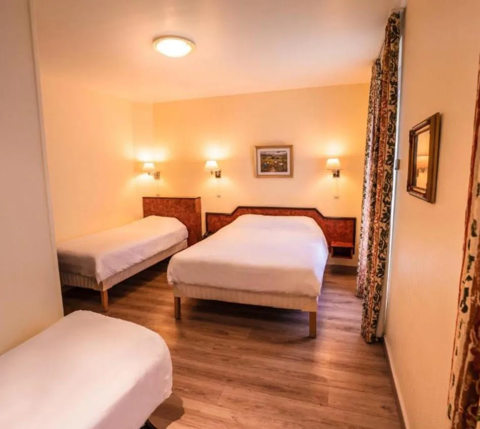 Chambre d'hôtel avec trois lits, décor chaleureuse et éclairage doux.