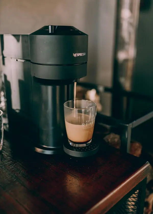 Machine à café noire faisant couler un espresso dans une tasse transparente posée sur une table.