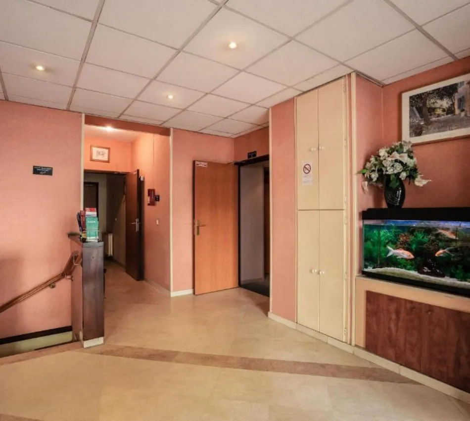 Un hall avec aquarium, fleurs et portes ouvertes, murs roses et plafond à dalles.